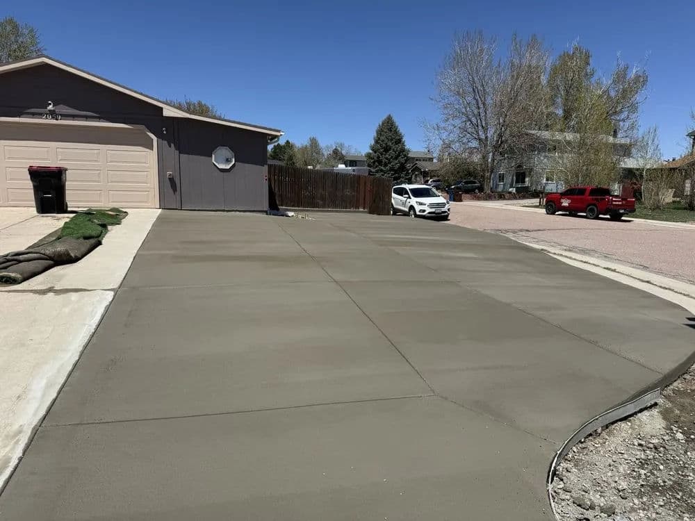 Freshly poured concrete driveway with a house in the background and a clear blue sky.