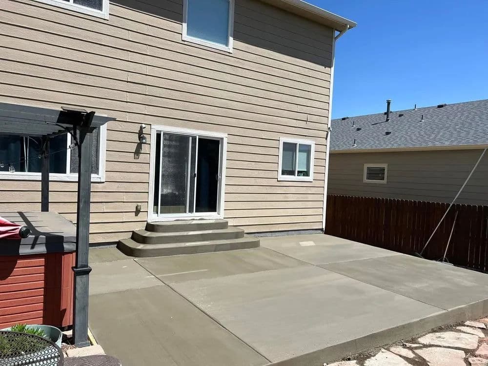 Newly poured concrete patio in backyard with sliding glass door and wooden fence.