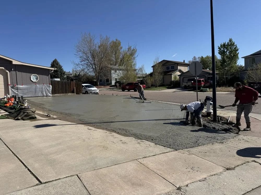 Crew pouring and finishing concrete on a residential driveway on a sunny day.
