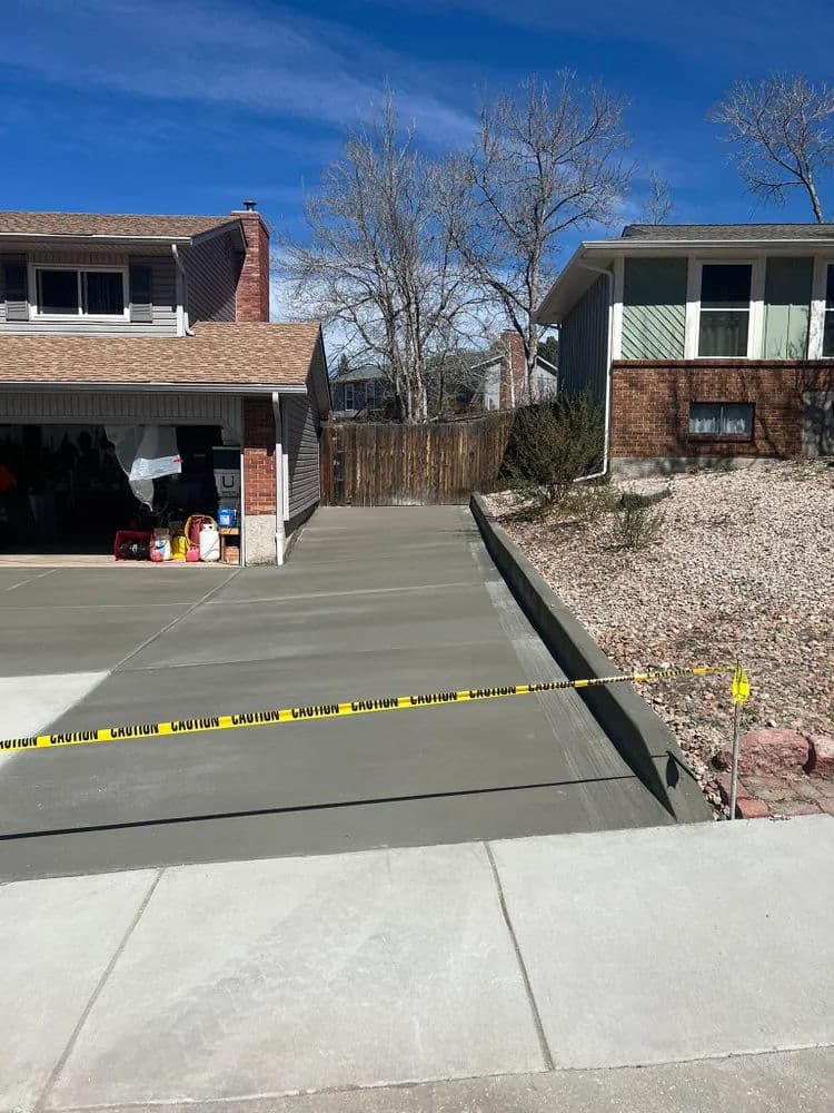 Freshly poured concrete driveway with caution tape, residential homes in the background.
