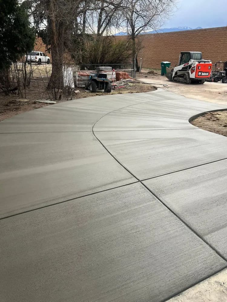 Freshly poured concrete driveway with construction equipment in background and landscaping.
