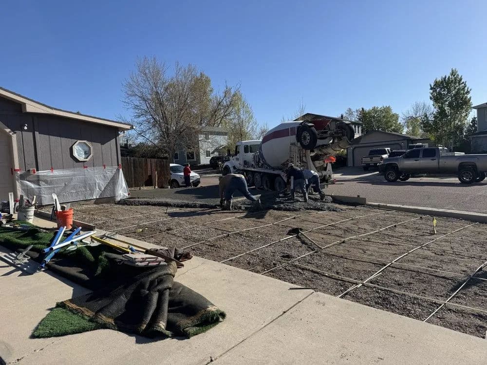 Concrete pouring process in residential driveway construction with workers and machinery.