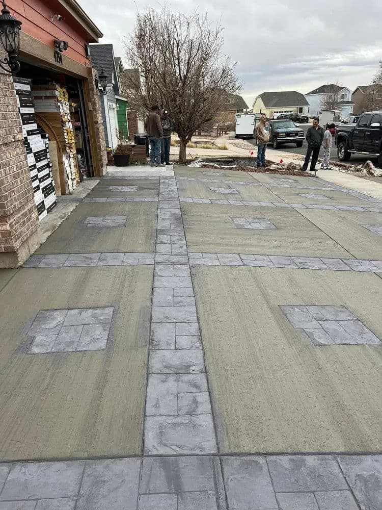 Concrete driveway installation with patterned surface and construction workers on site.