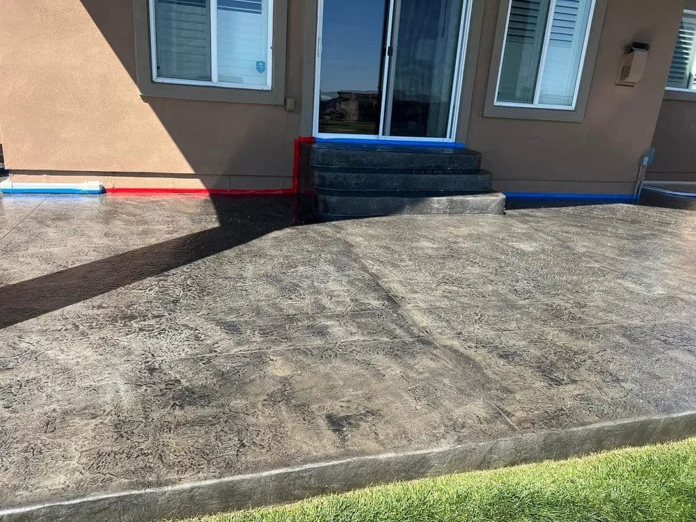 Decorative stained concrete patio with steps and colorful borders outside a home.