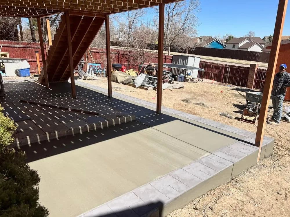 Concrete patio installation under a raised deck with construction tools nearby.