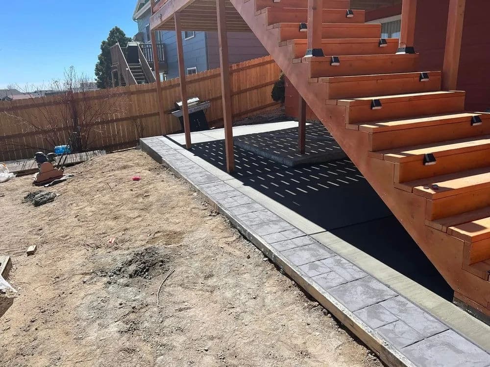 Wooden stairs leading to a patio with concrete paving and gravel landscaping.