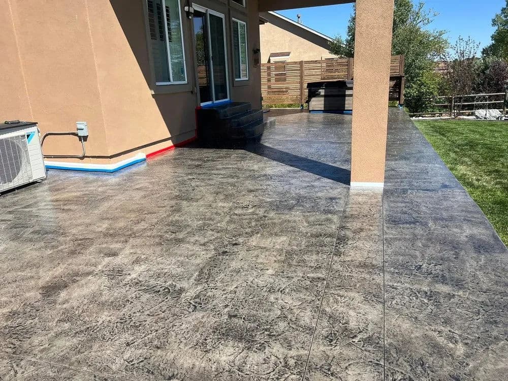 Decorative stamped concrete patio beside a house with air conditioning unit and green lawn.