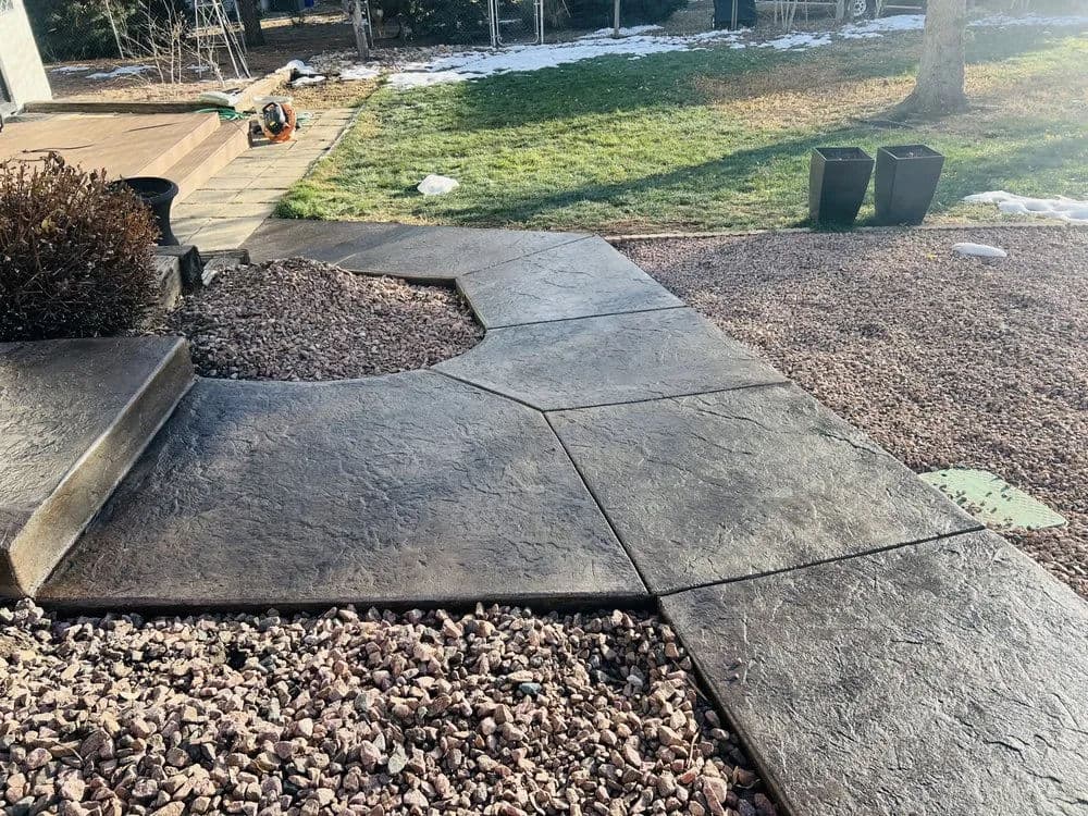 Textured patio with a curved walkway, gravel landscaping, and snow-covered grass.