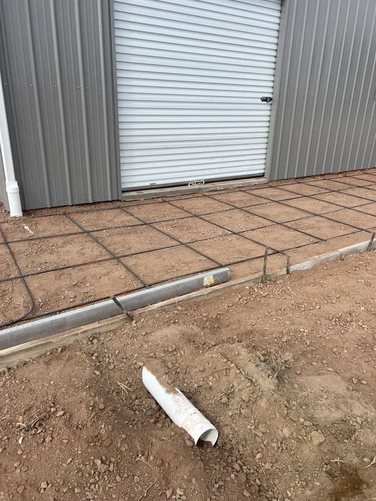 Concrete slab preparation with rebar grid near a storage building entrance.