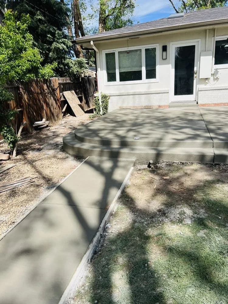 Freshly poured concrete patio and walkway in a backyard surrounded by trees.